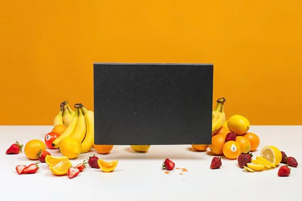 Black laptop surrounded by bananas and oranges on orange