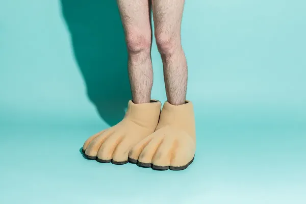 Bare legs wearing giant chimp-feet slippers on a teal backdrop