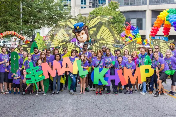 Mailchimp team marching in a Pride parade with giant letters spelling Mailchimp and a Freddie float