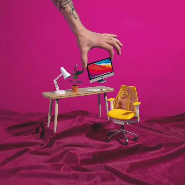 A hand placing a tiny desk, chair and computer on pink fabric